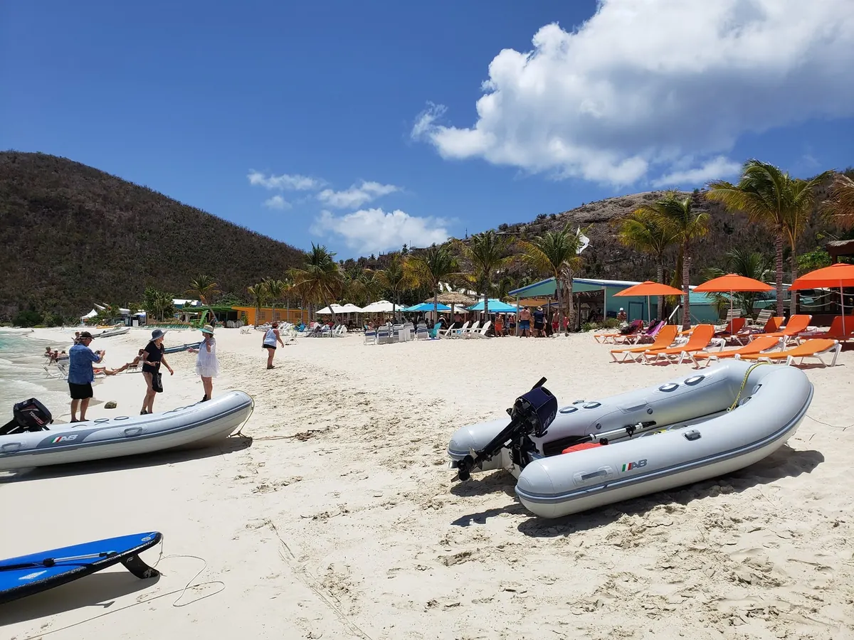 Beachgoers and two inflatable tender boats on the sand at White Bay, Jost Van Dyke, below a green hillside.